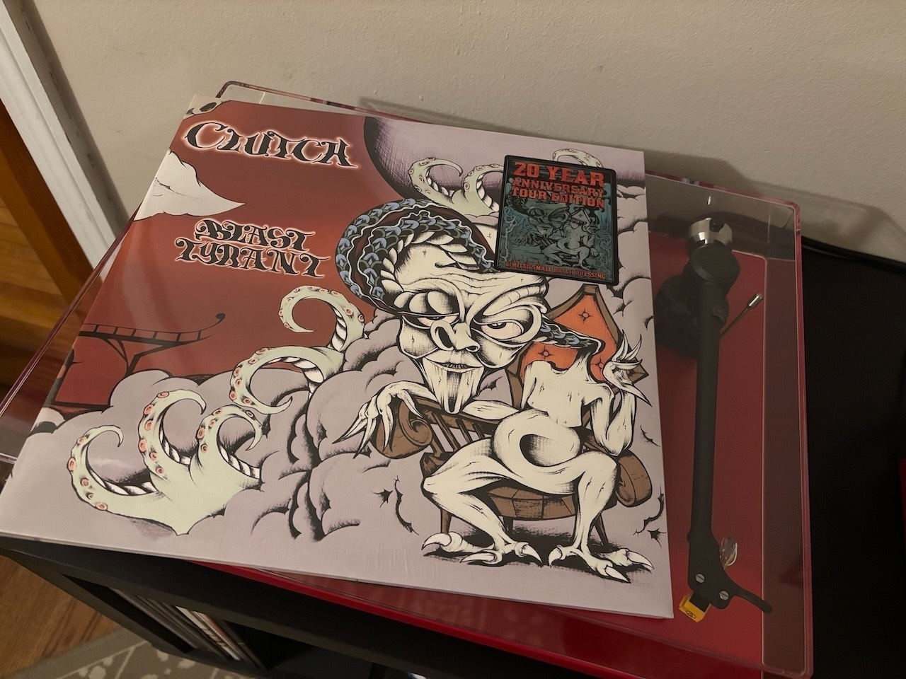 Auto-generated and human edited description: Blast Tyrant by Clutch record with a fantasy-themed cover featuring a dragon-like figure and a “20 Year Anniversary Tour Edition” sticker is placed on a turntable.